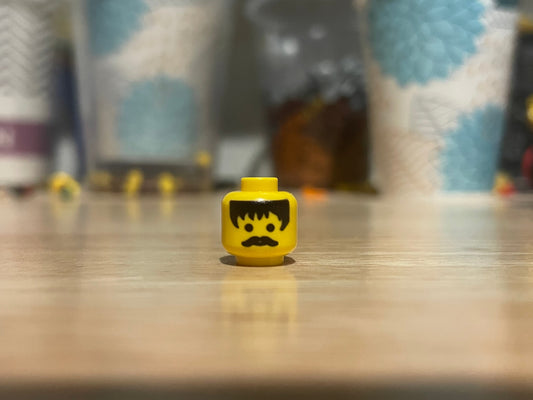 LEGO minifigure black hair head with mustache on wooden surface