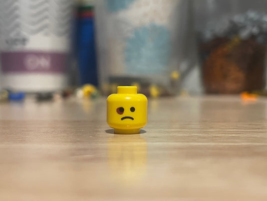 LEGO minifigure yellow head with black eye and sad expression on wooden surface