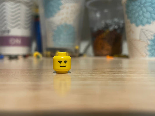 Yellow LEGO minifigure head with Southern Smile face on wooden surface
