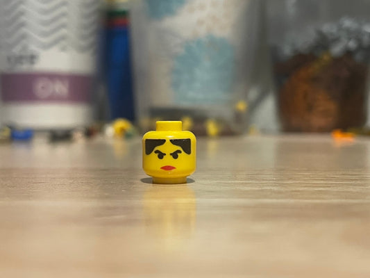 LEGO Western Female #1 minifigure head with eyebrows and red lips on wooden surface