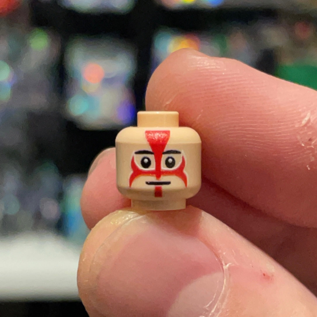 Close-up of a hand holding a LEGO Thug Head minifigure face with red and black markings