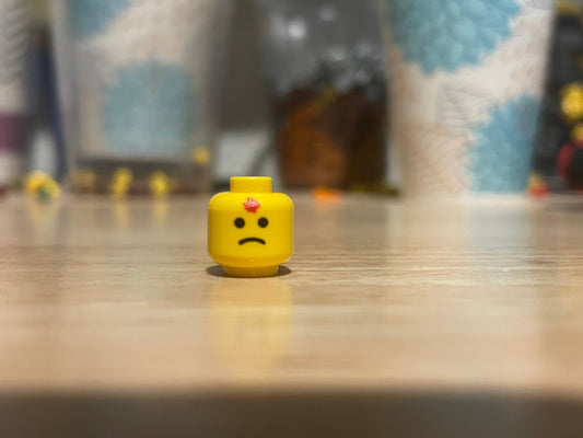 LEGO headshot head with a sad face on wooden surface and blurred background
