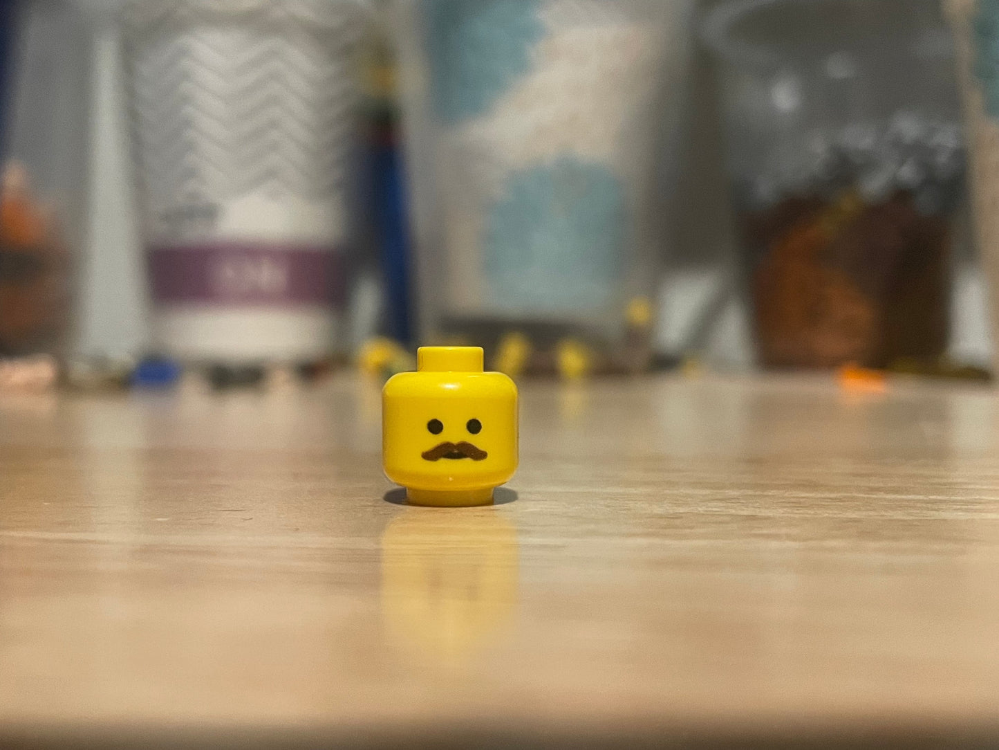 LEGO minifigure yellow head with a brown mustache on a wooden surface
