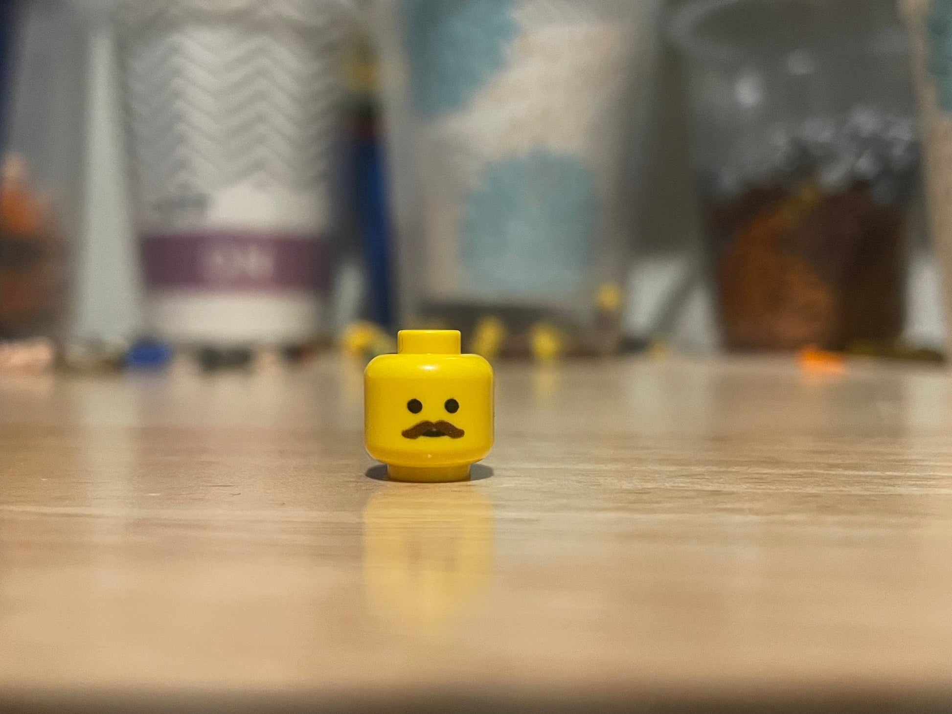 LEGO minifigure yellow head with a brown mustache on a wooden surface